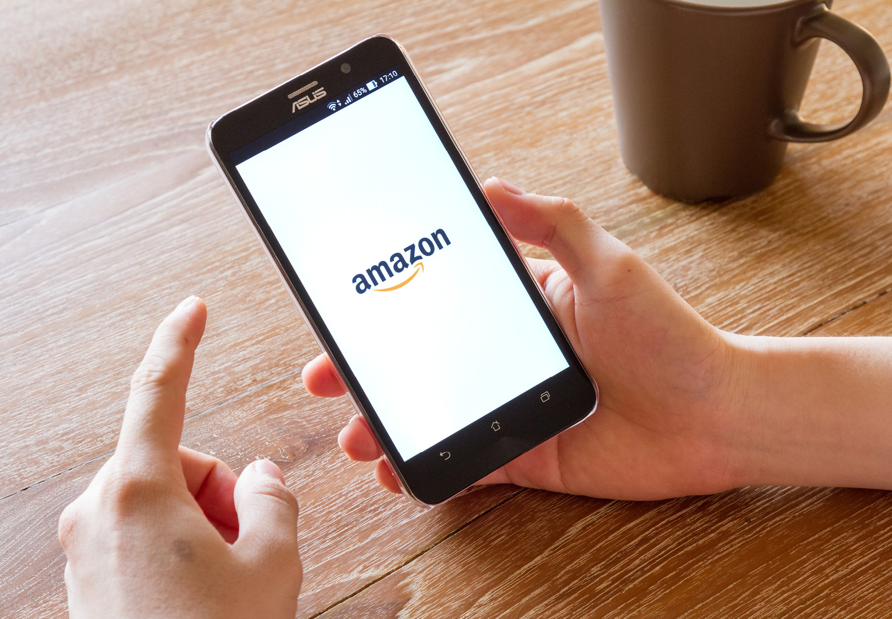 Closeup image of hands using a phone with the Amazon.com logo on the screen. Stock photo.