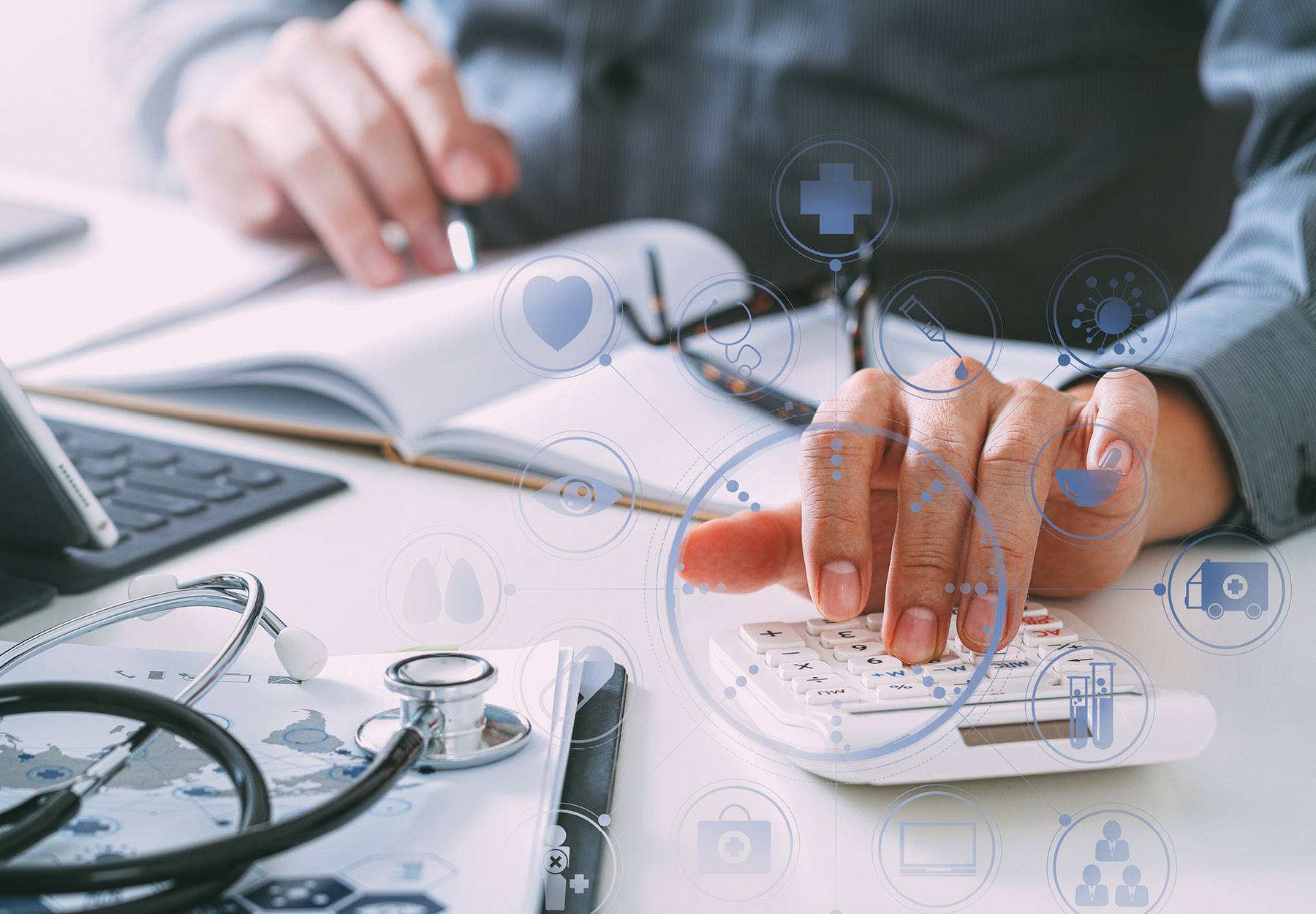 Closeup of someone using a calculator while writing in a notebook on a white desk. A stethoscope sits on the desk nearby. There is a graphical overlay of healthcare and medical lab symbols. Stock photo illustration.