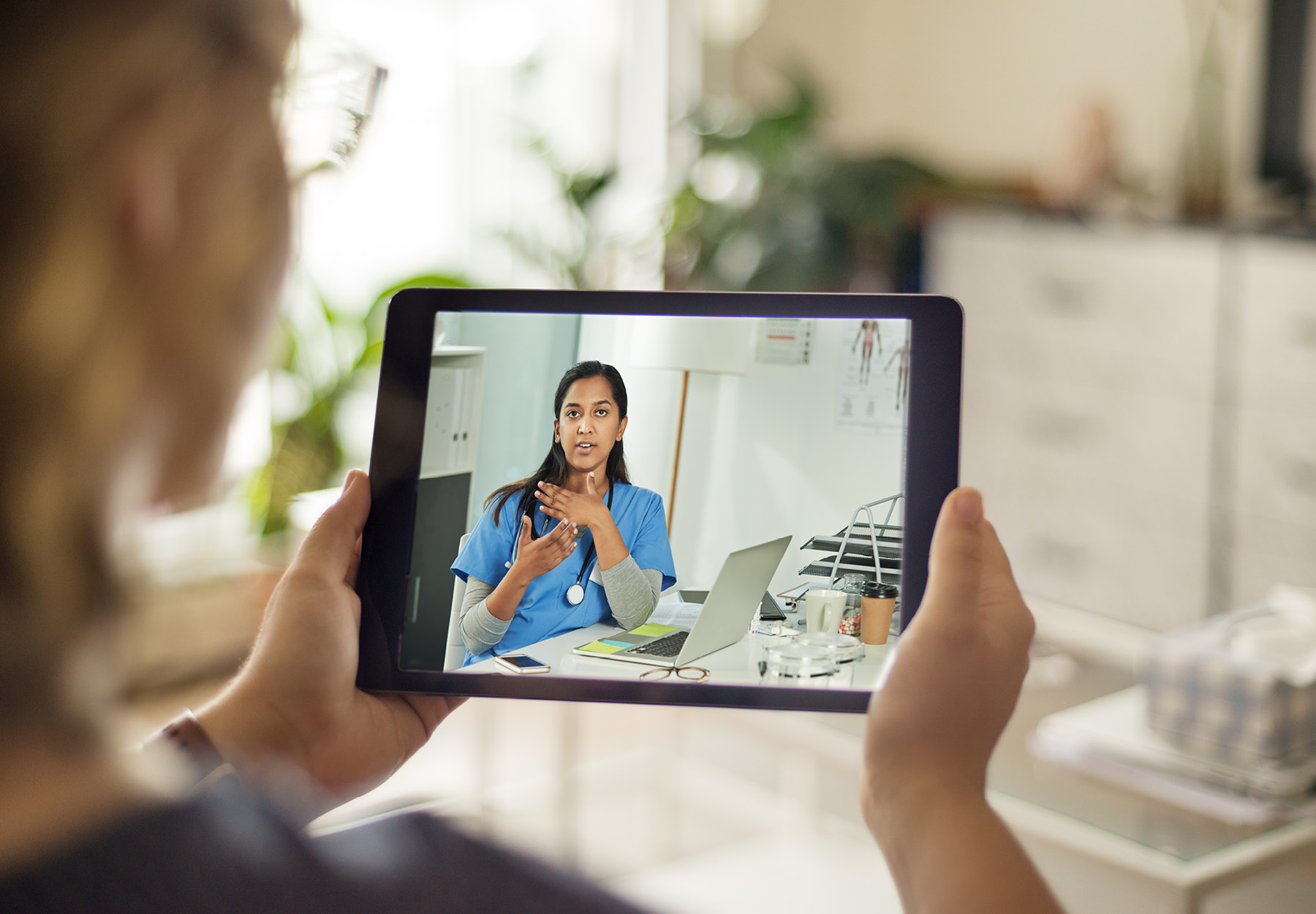 Woman holding tablet showing a video call with her female doctor. Stock image.