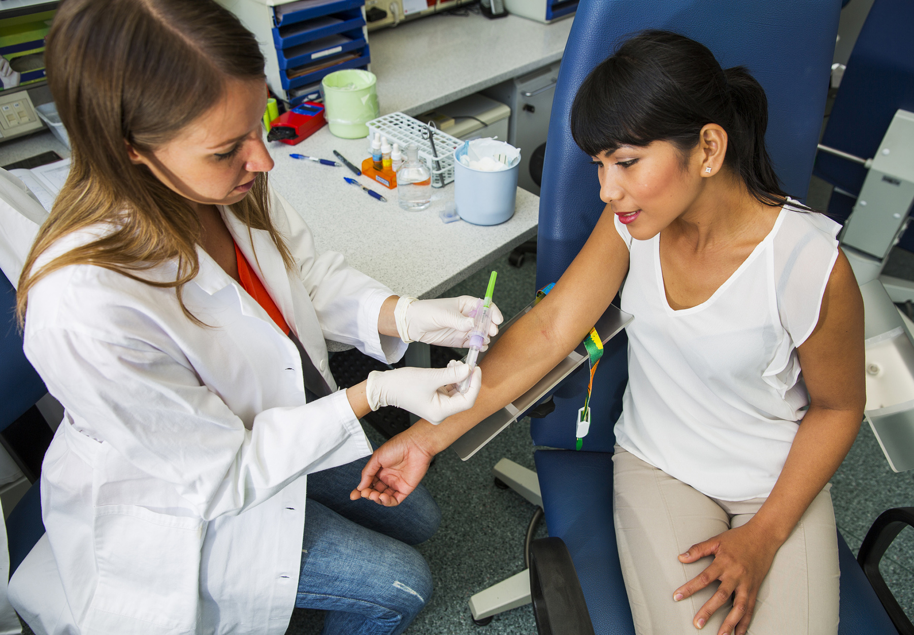 Female healthcare worker prepares a female patient for a blood draw. Stock photo.