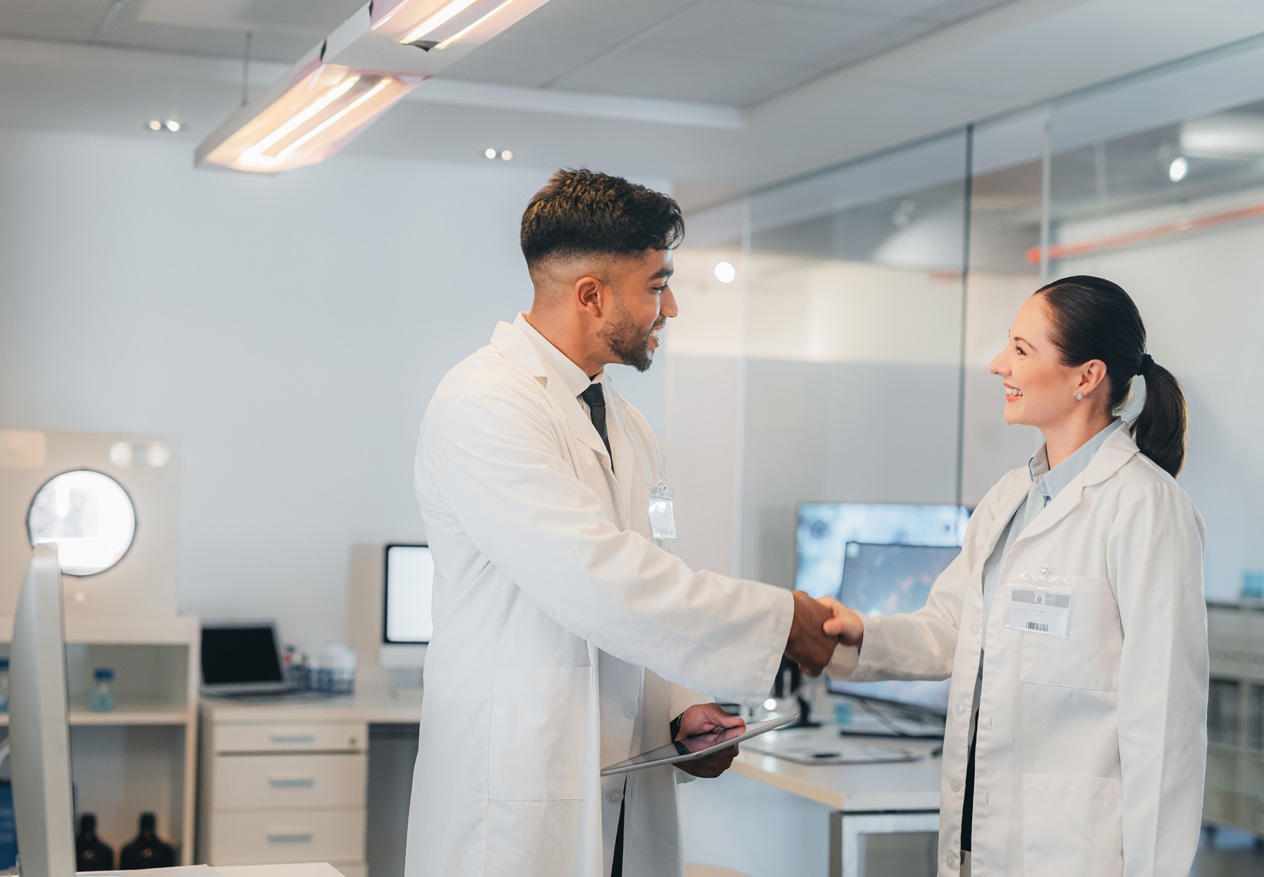 A male lab staffer shakes the hand of a new female lab employee. Stock photo.