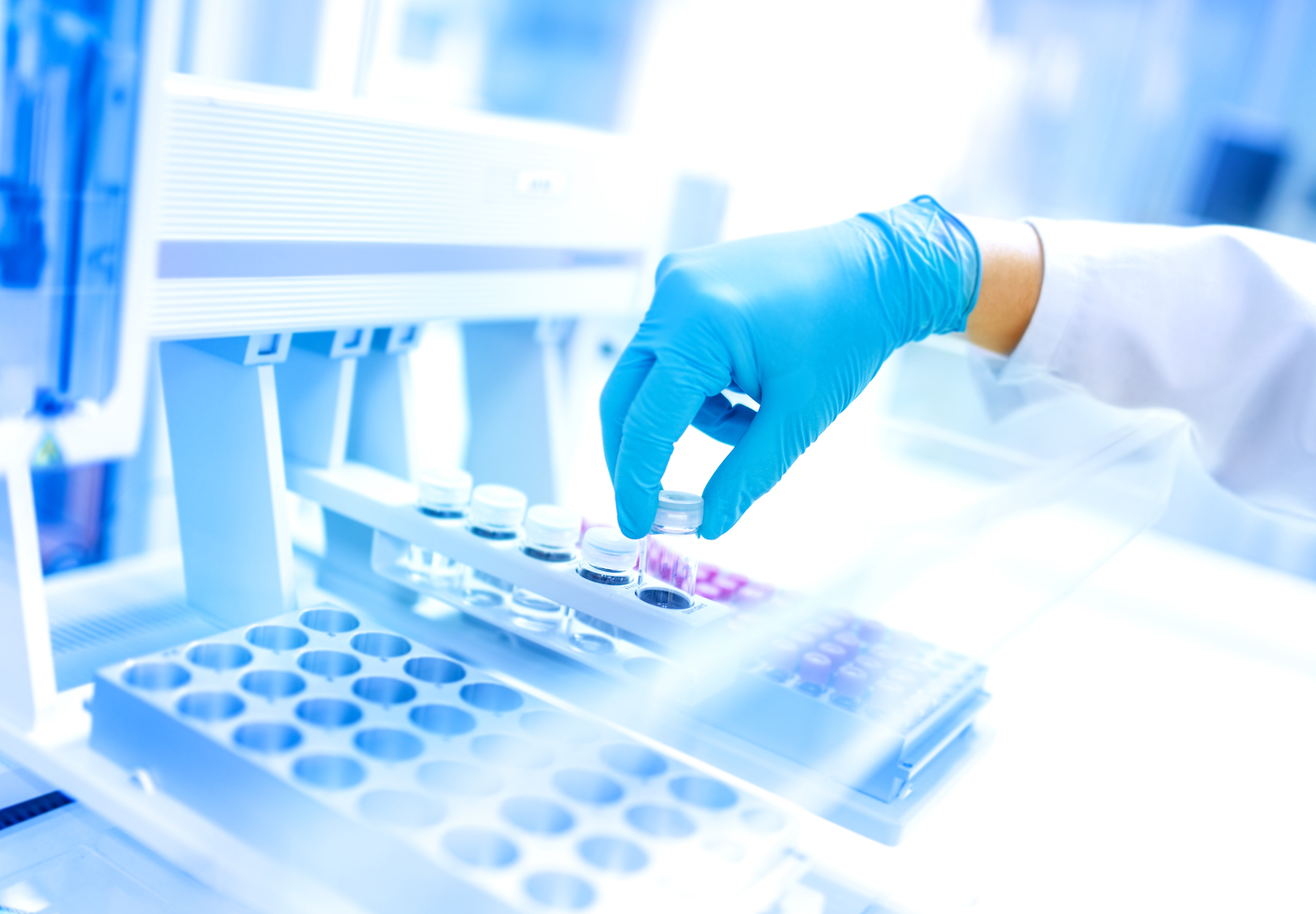Closeup of gloved hand of lab worker loading clinical lab machine. Blue and white tones. Stock photo.