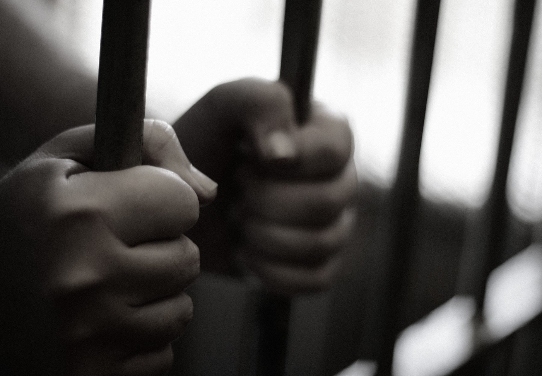 Black and white closeup photo of hands holding bars of a prison cell. Prison time concept. Stock image.