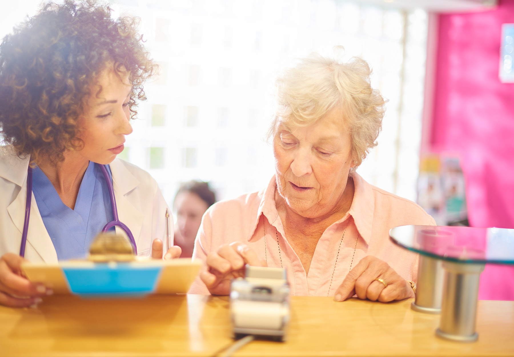 Senior white female patient paying her medical bill at front desk of doctor's office. The woman's female African American doctor is standing next to her, helping with the payment process.