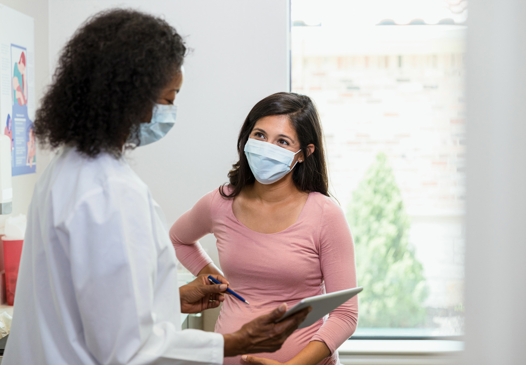 Pregnant woman of Hispanic descent meets with her female, African American doctor. iStock image.