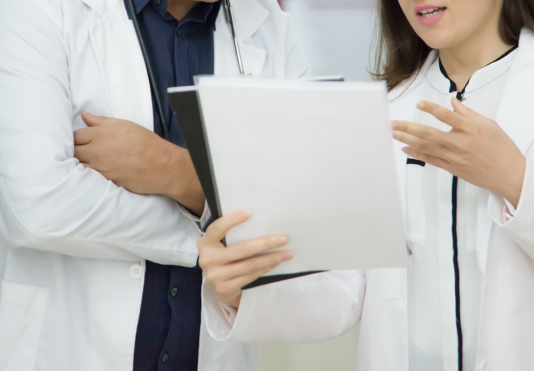 Doctor meeting with laboratory professional who is holding a document. Stock photo.