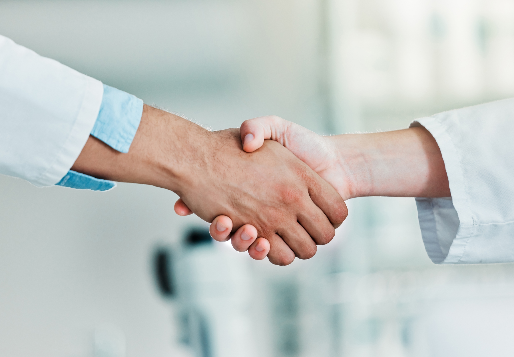 Closeup of two lab workers shaking hands. One hand has a white skin tone and one hand has a tan skin tone. Stock image.