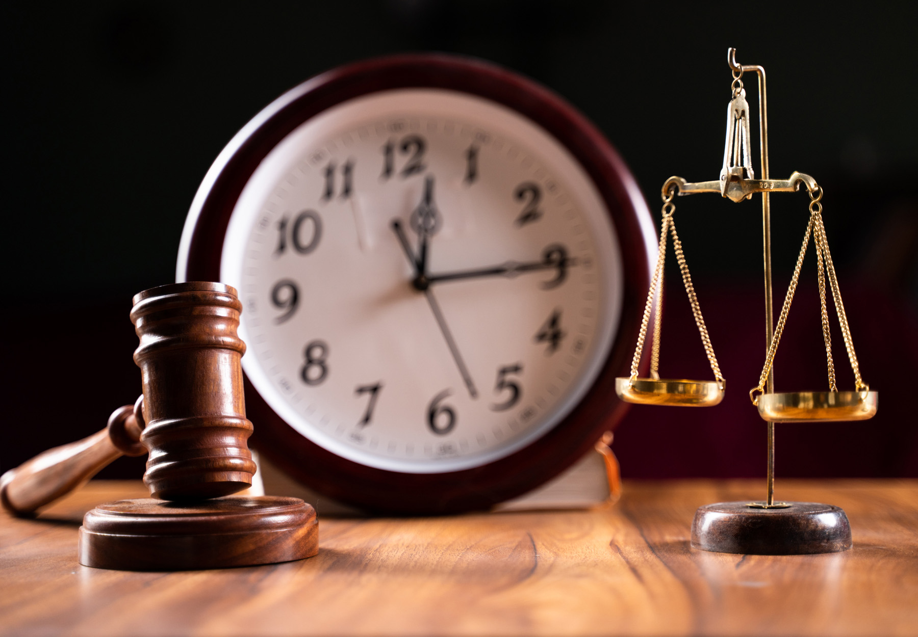 Image of gavel and scales on a wooden table with a clock in the background. Court delays concept. Stock image.