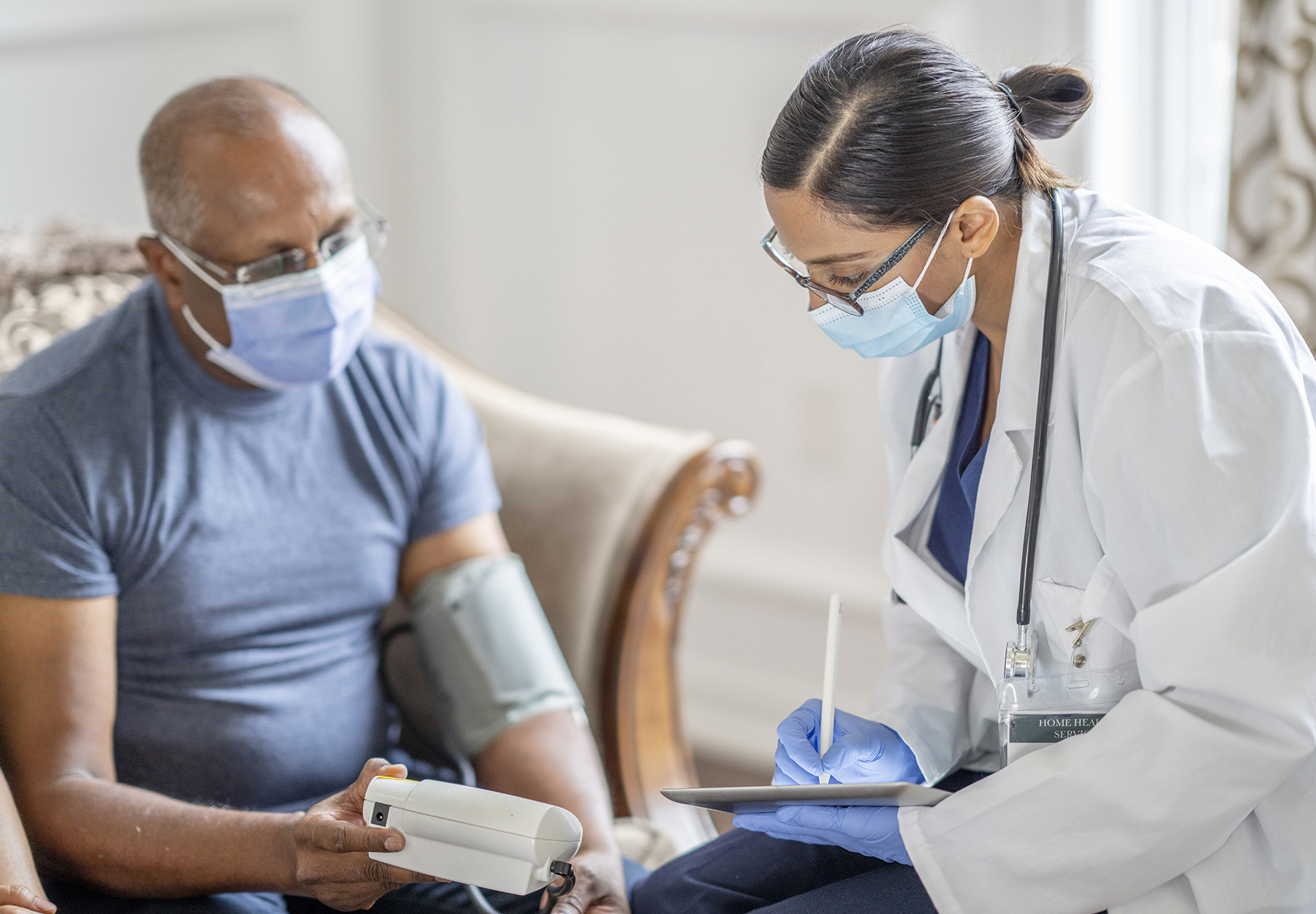 Female doctor meeting with male patient in his home. Taking blood pressure. iStock image.