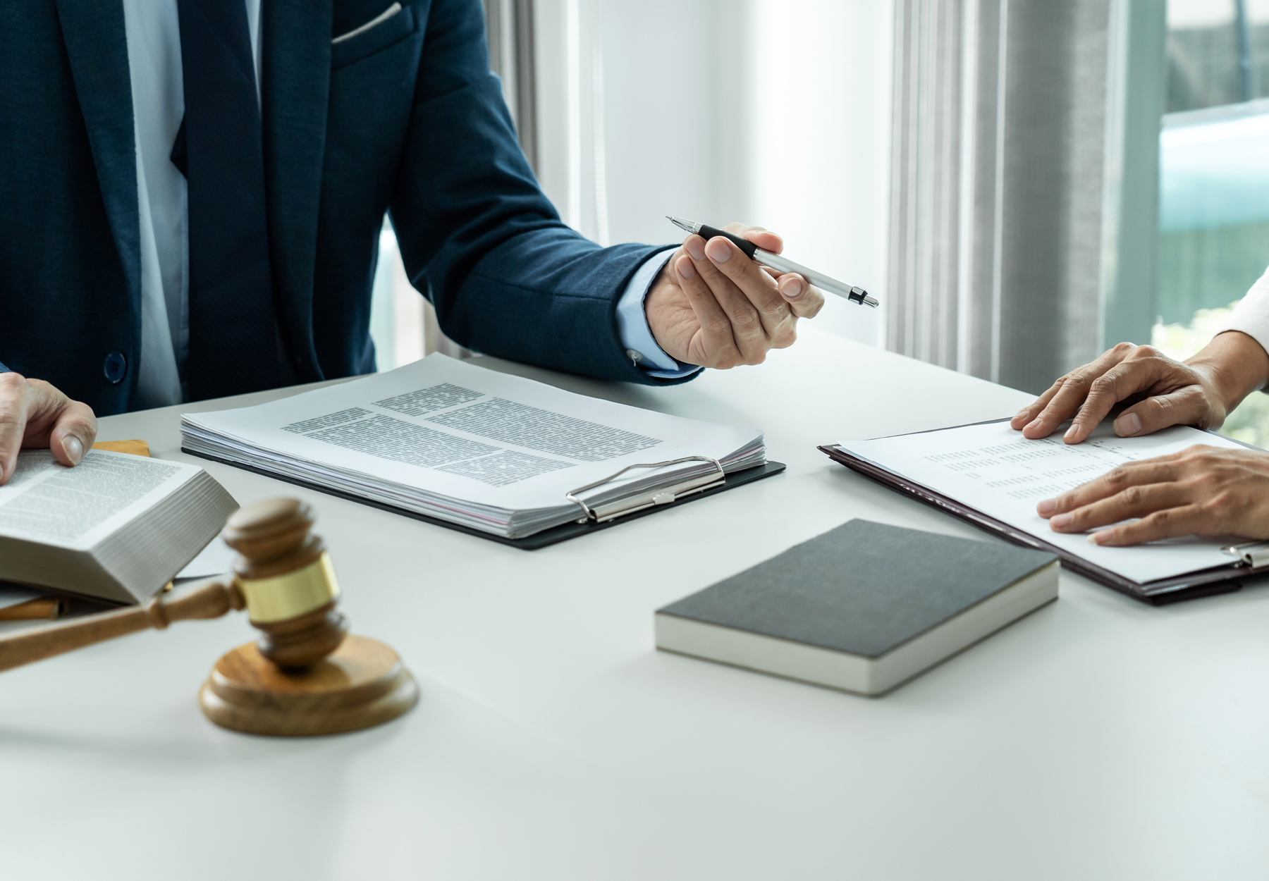 Closeup of lawyer and lab professional meeting at a white desk with books and papers and a gavel on it. iStock image.