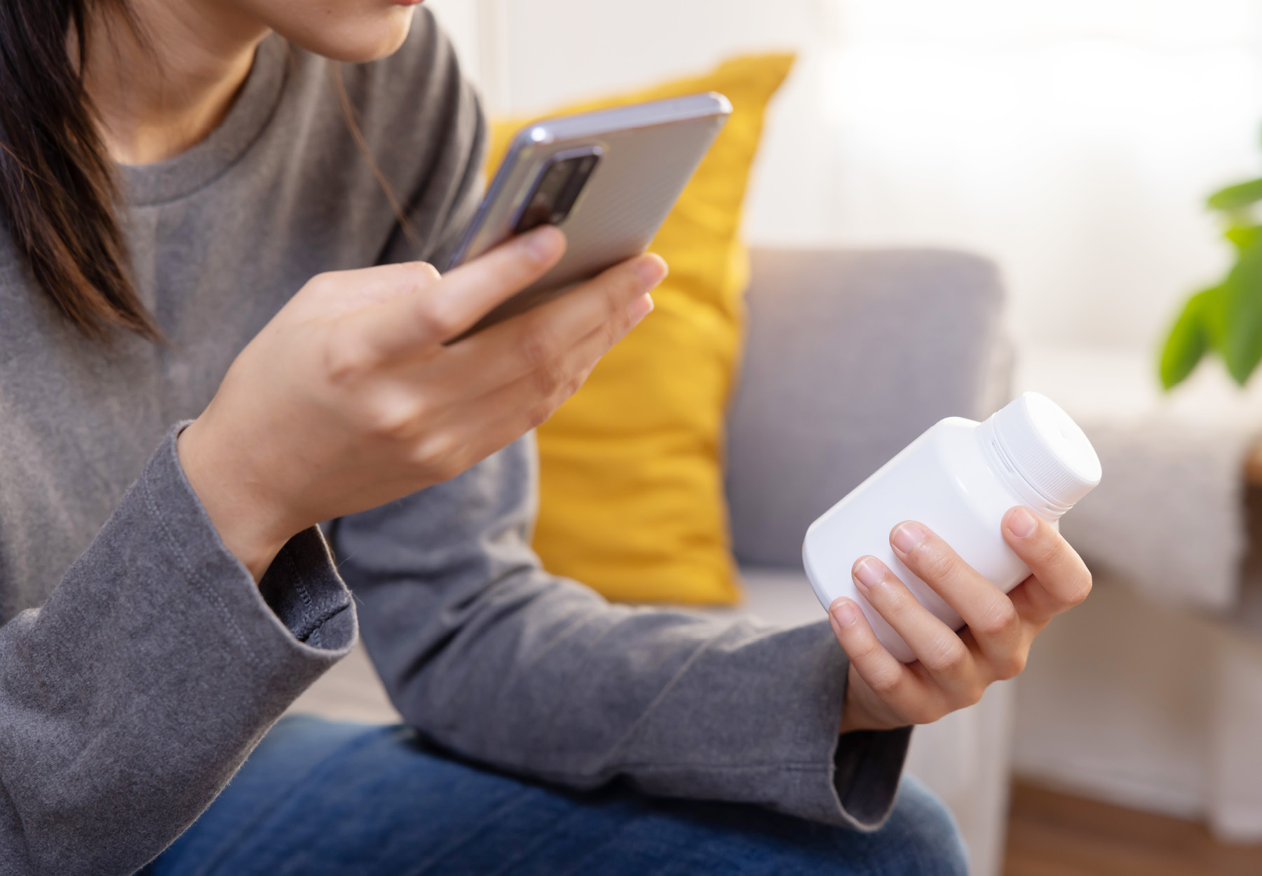 Closeup of woman texting on phone while holding bottle of prescription medication. iStock image.