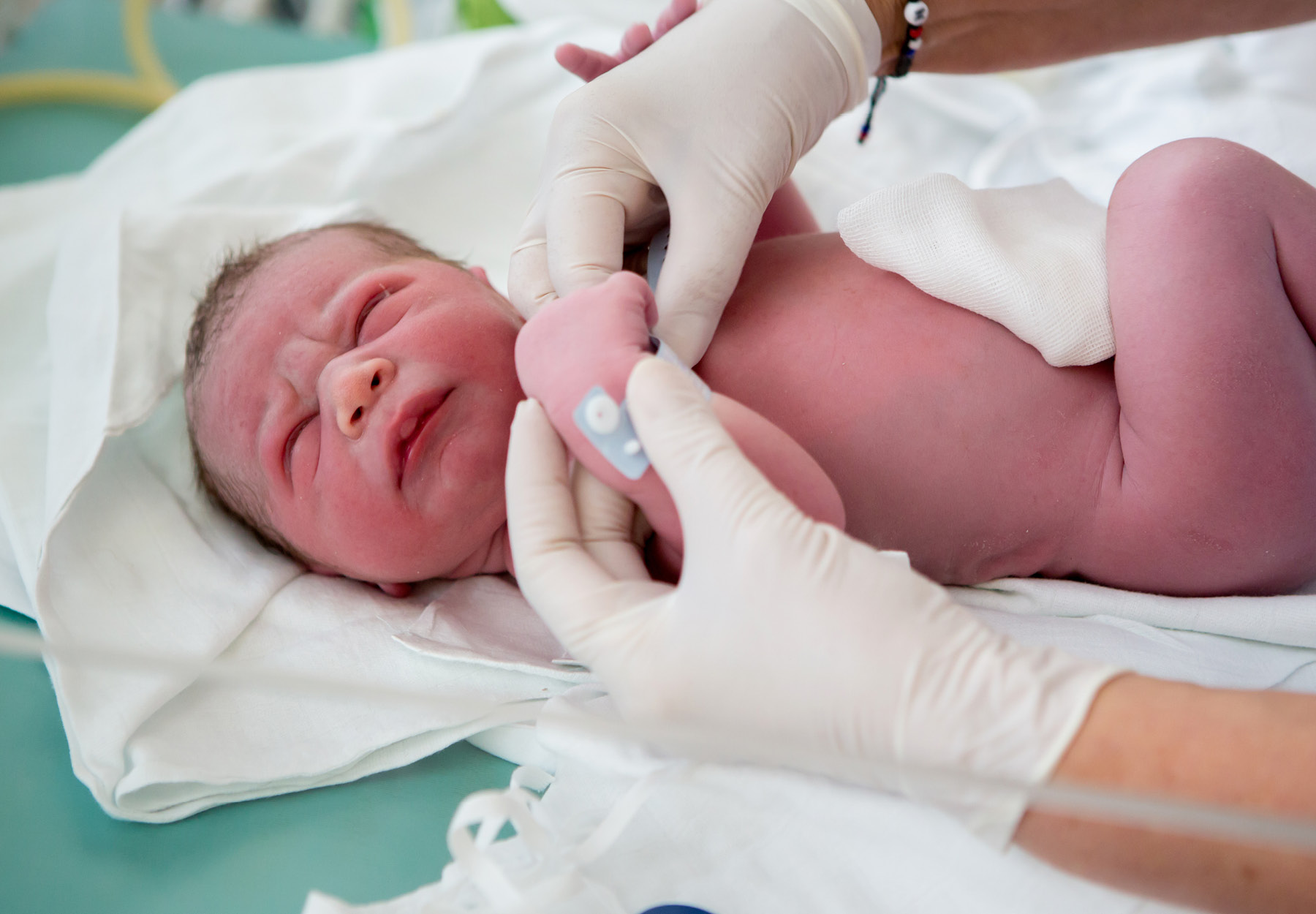 Image of newborn baby being examined by healthcare professional wearing white disposable gloves. iStock image.