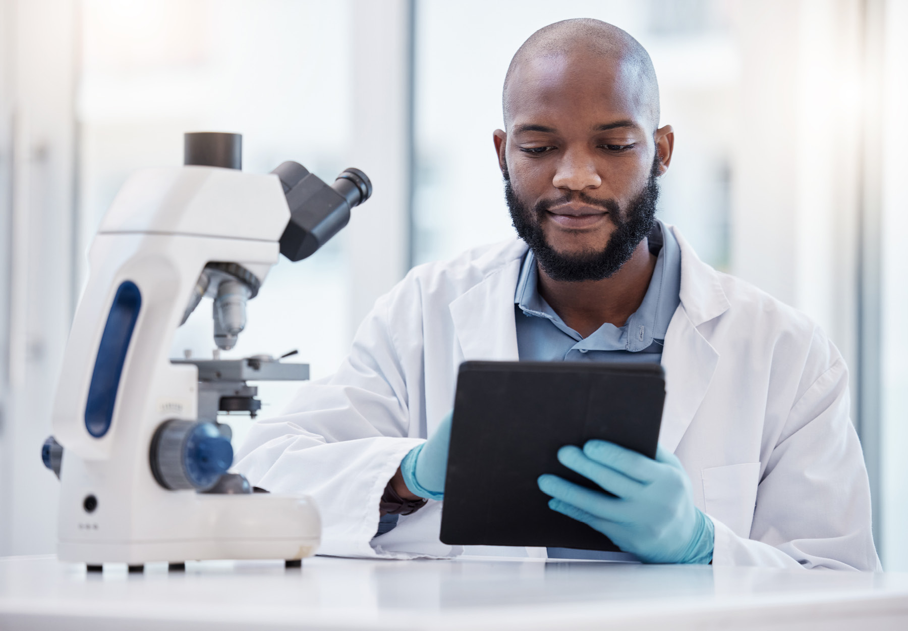 Clinical lab professional in lab coat and gloves working on a tablet. iStock image.
