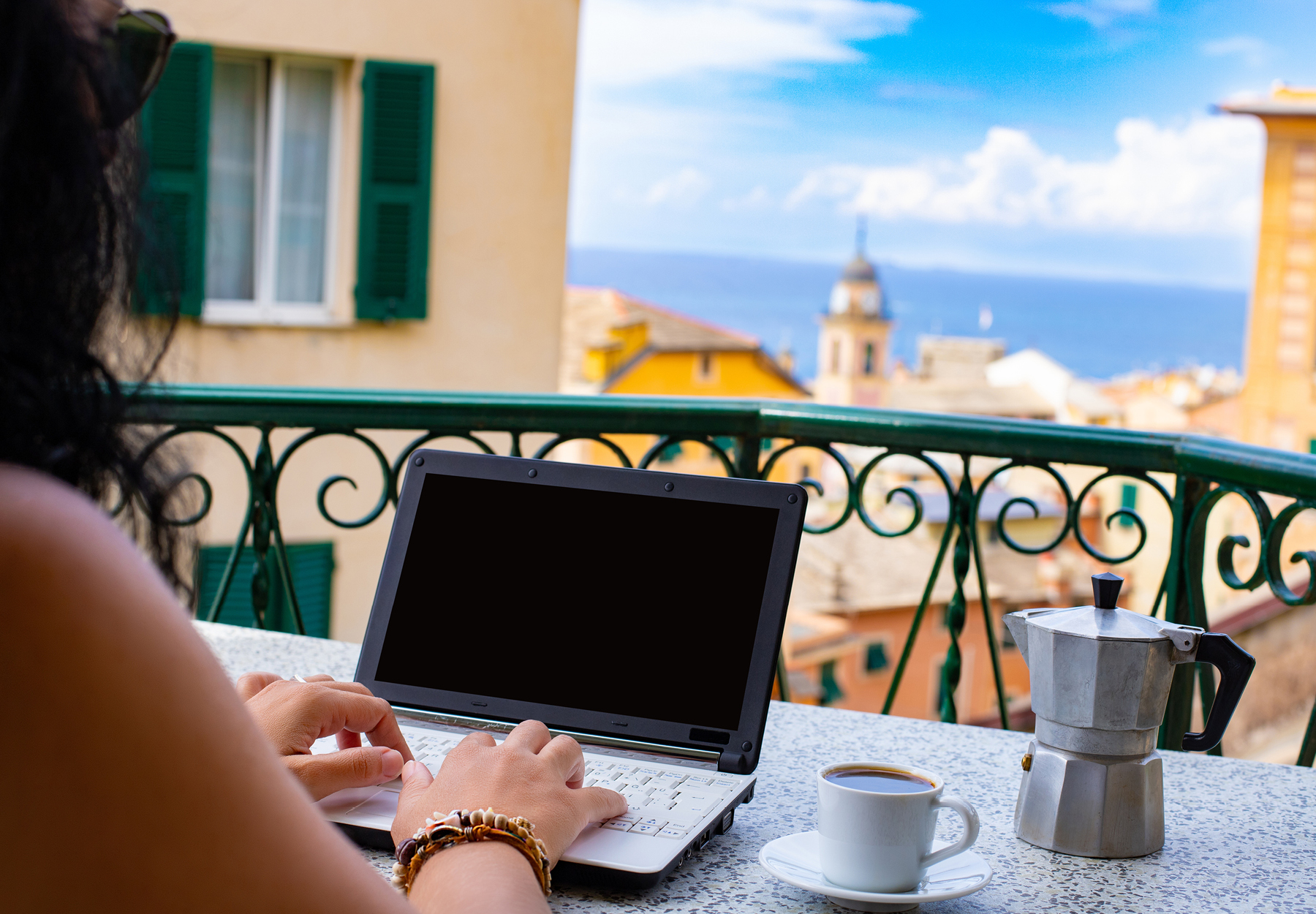 Closeup of someone's hands typing on a laptop from a balcony that has an ocean view. Digital nomad concept. iStock image.