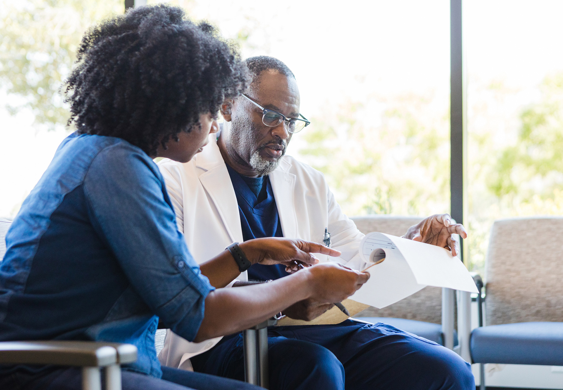 An African American male doctor meets with a female African American patient, looking at notes. iStock Image.