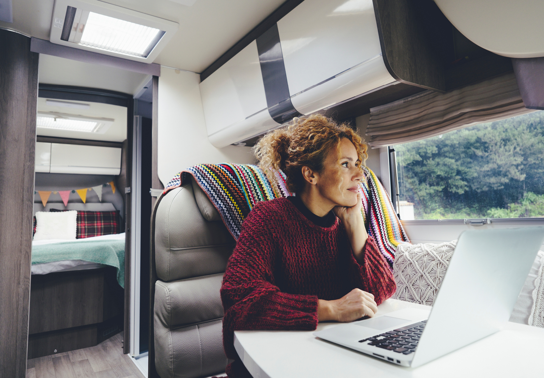Woman working remotely on her laptop at a table in her recreational vehicle. iStock image.