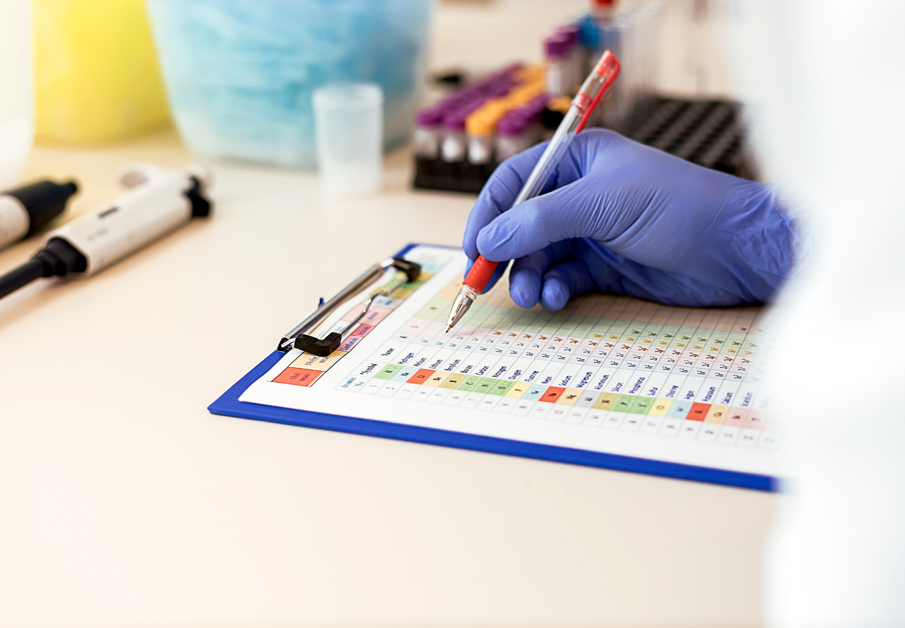 Closeup of clinical lab professional in PPE writing in a clipboard. iStock image.