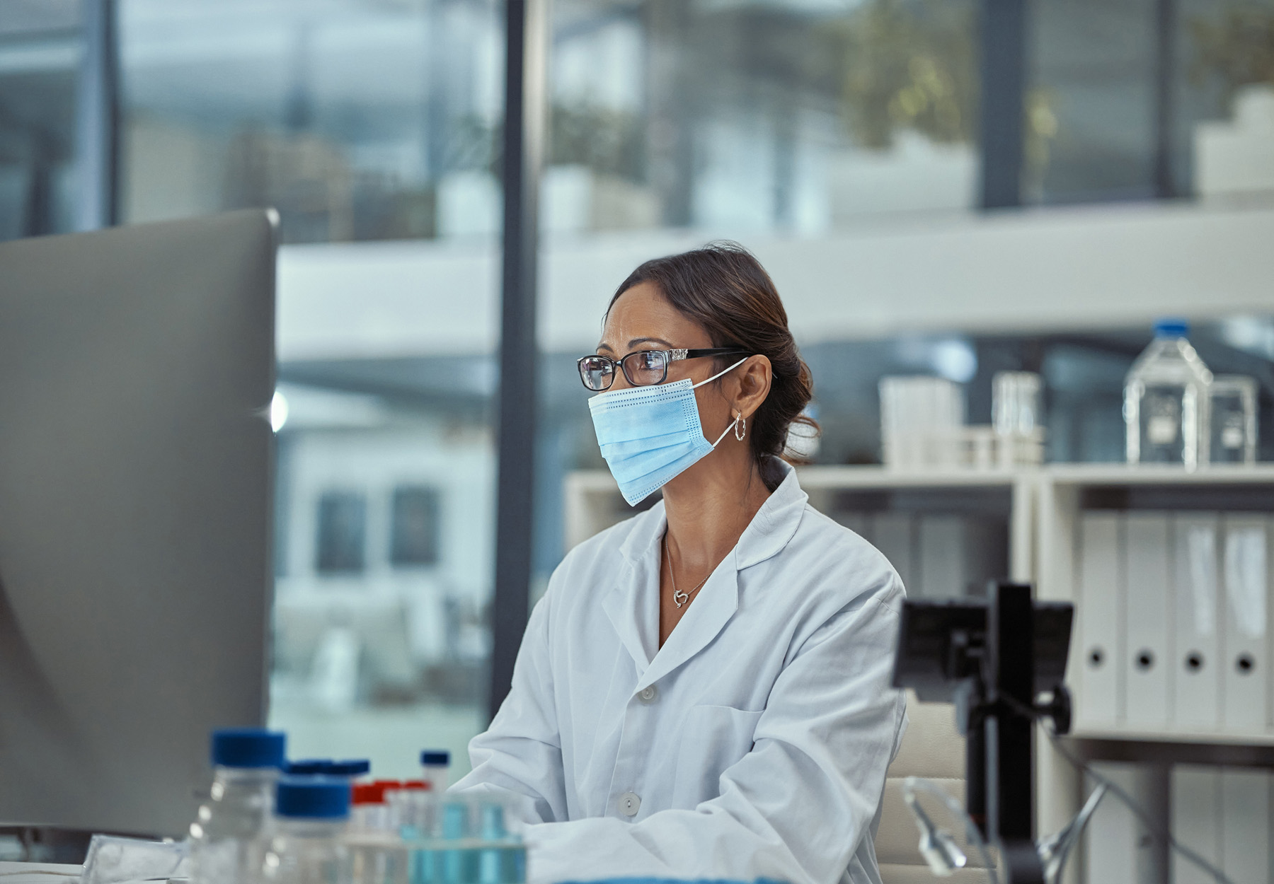 Female laboratory professional in full PPE works on a computer in the lab. iStock image.
