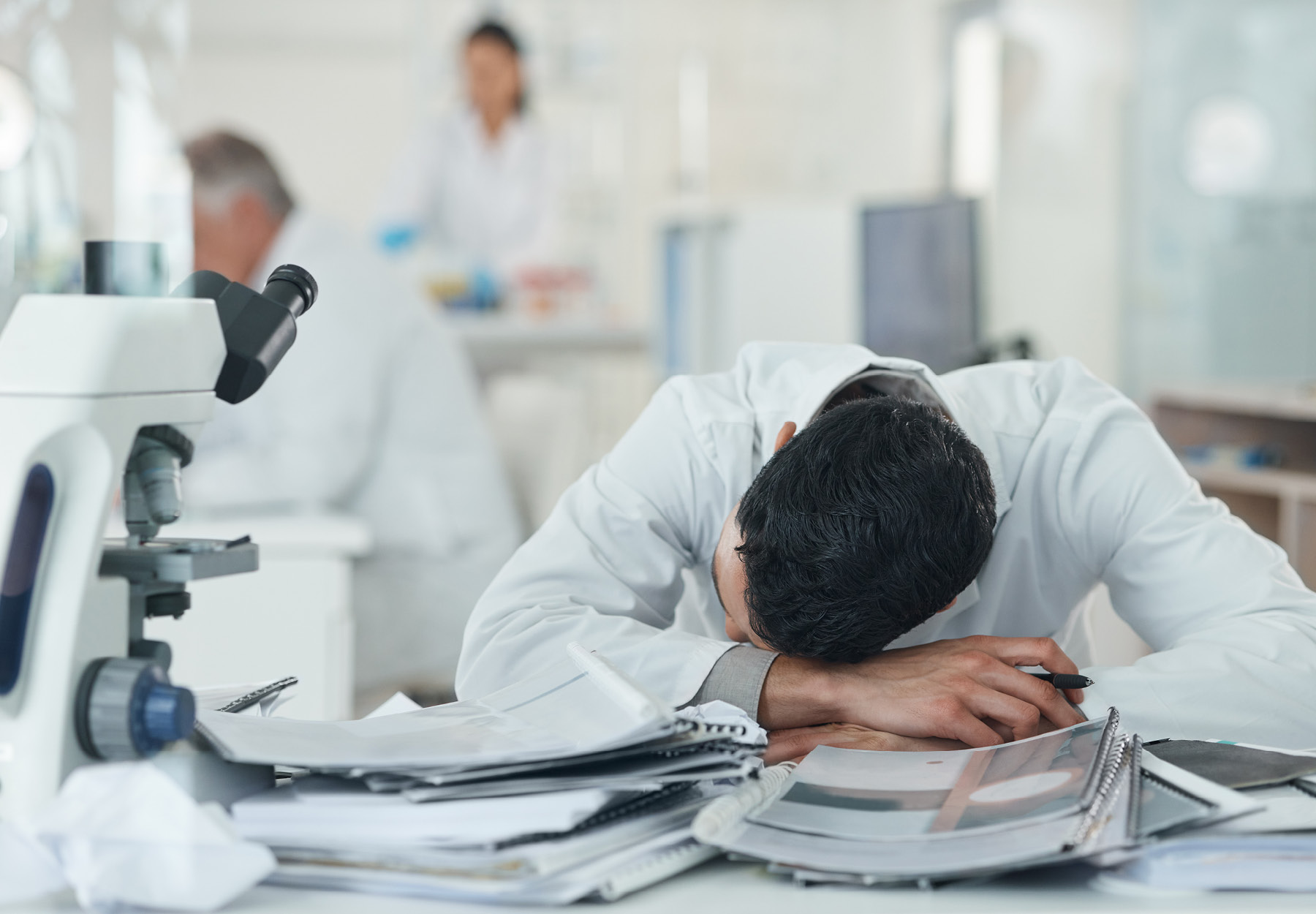 A stressed lab worker rests his head on a stack of papers on the lab bench. iStock image.