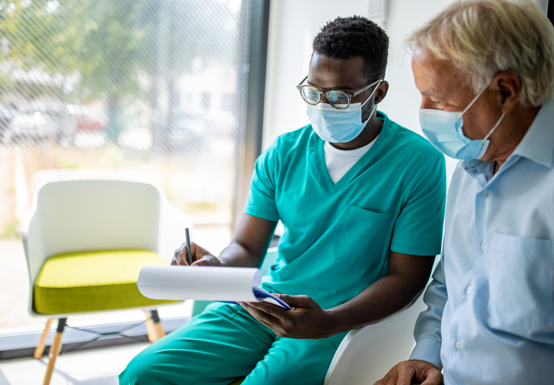 A young, male African American hospital staff member meets with an elderly White male patient. iStock image.