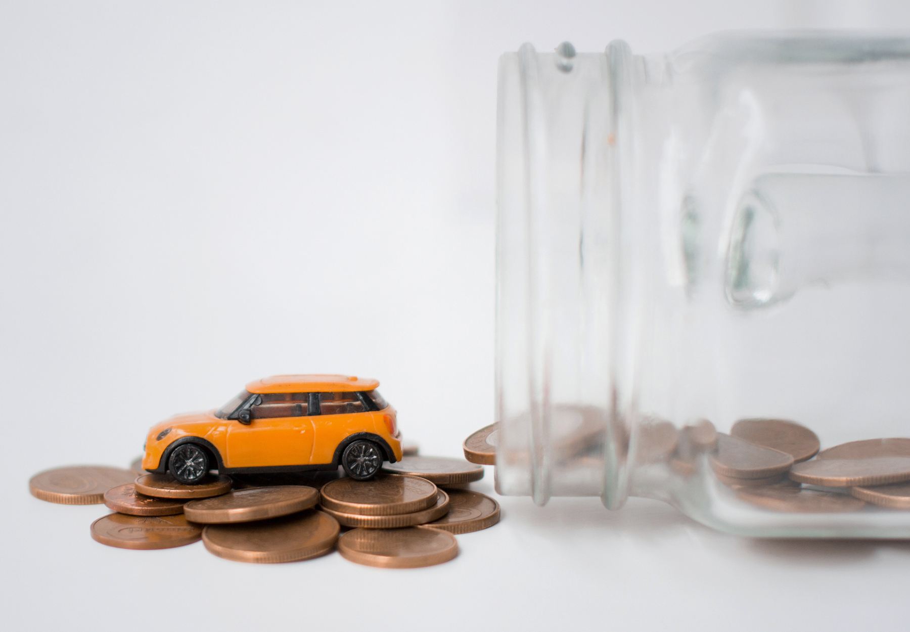 An orange model car rests on coins spilling from a jar. Travel allowance concept. iStock image.