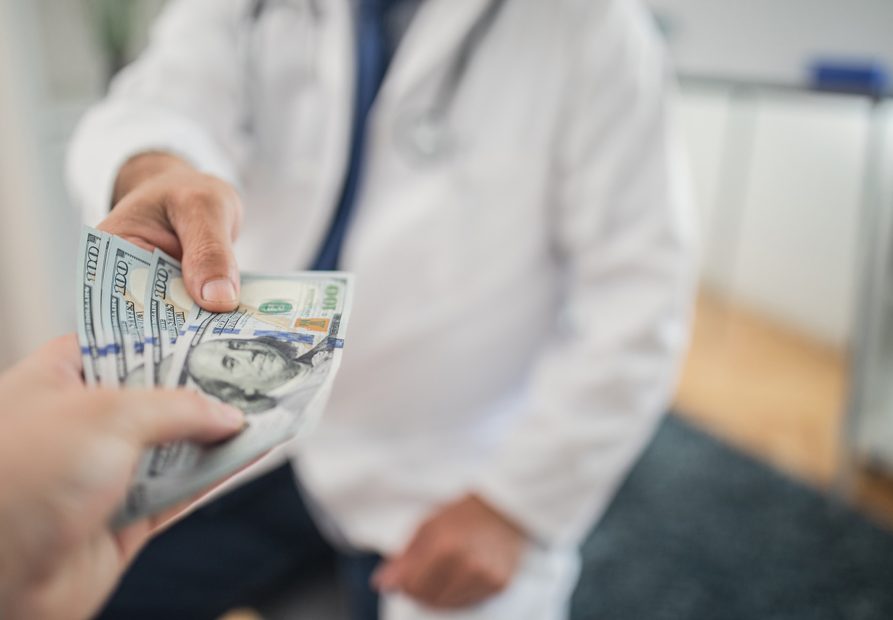 Closeup of someone giving money to a doctor. Healthcare industry kickbacks concept. iStock image.