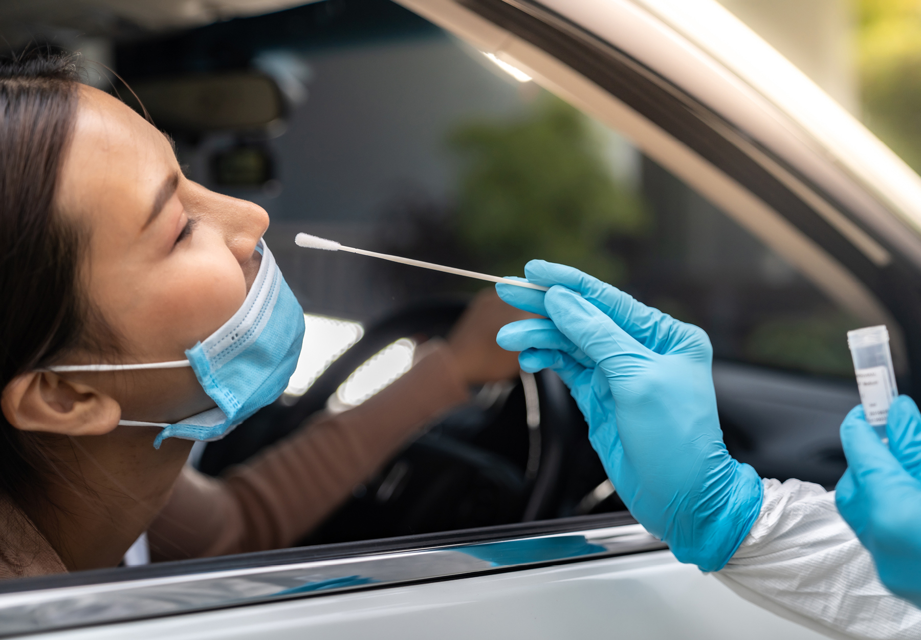 Closeup of woman receiving a nasopharyngeal swab from the front seat of her car during a drive-thru COVID-19 test. iStock image.