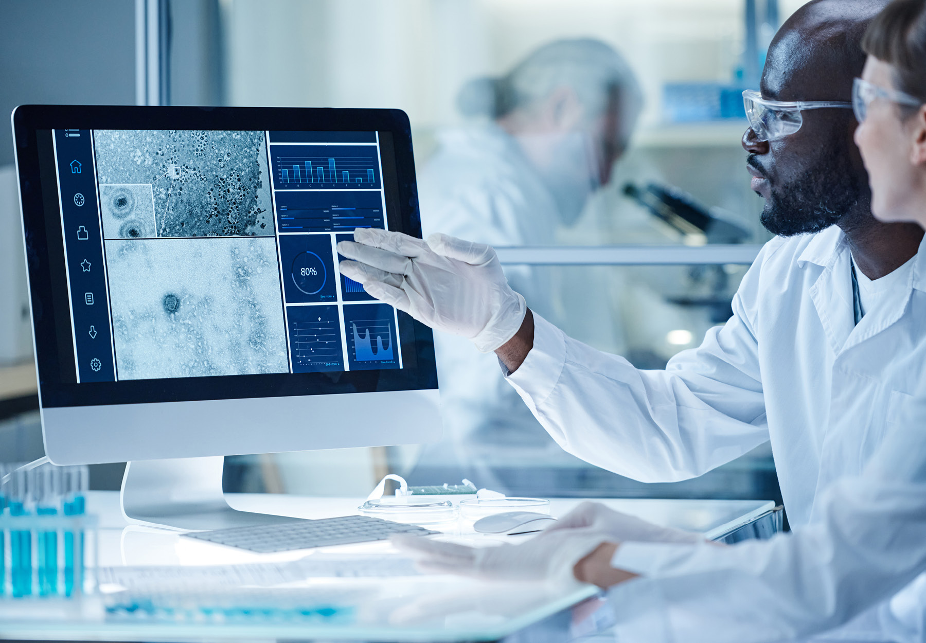 Gloved lab technician pointing to cancer analysis on a computer screen wearing safety glasses iStock Image