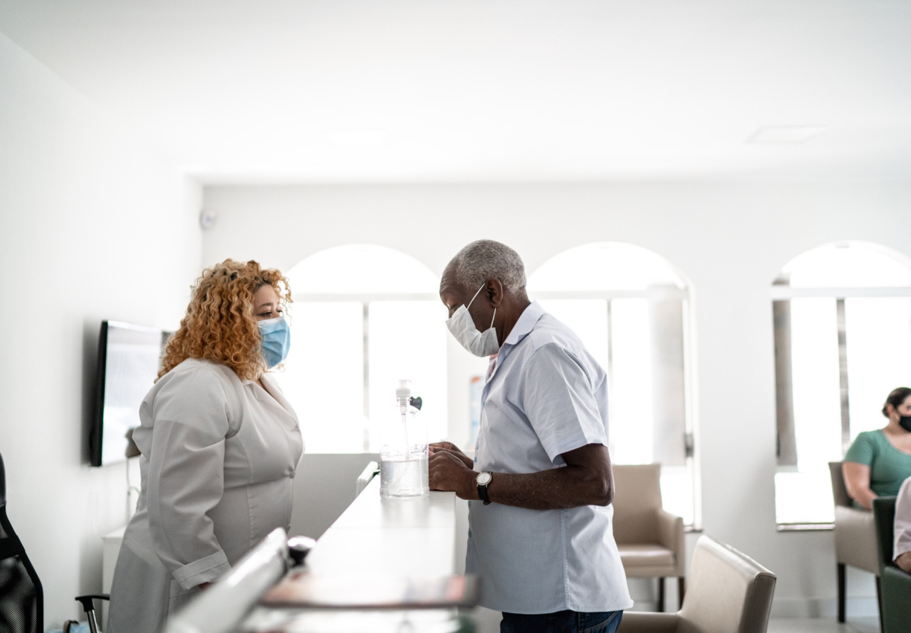 Medical clinic reception receptionist talking to patient using face mask iStock image