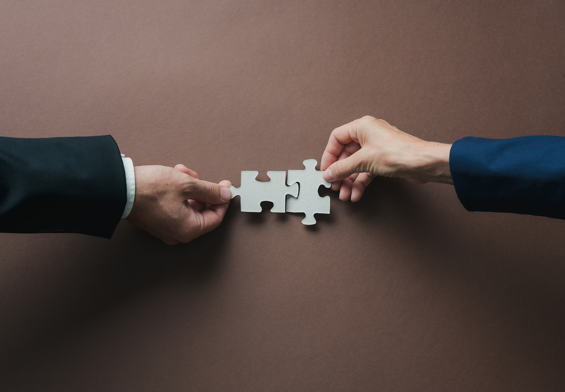 Closeup of hands of business people putting puzzle pieces together. Merger and acquisition concept. iStock image.
