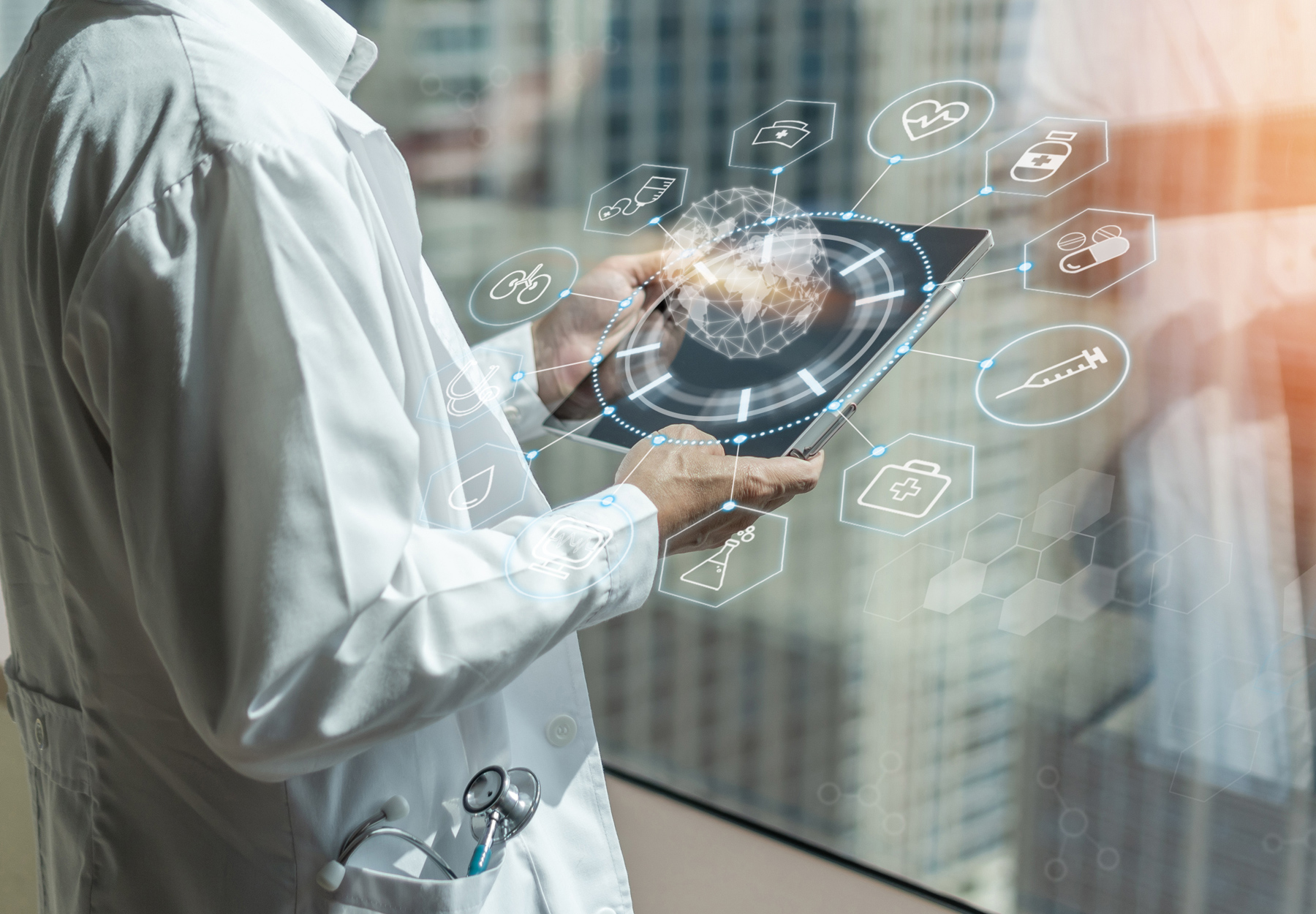 Closeup of doctor holding tablet with numerous medical icons. The doctor is at a window with a cityscape outside of it. Healthcare industry concept. iStock image.
