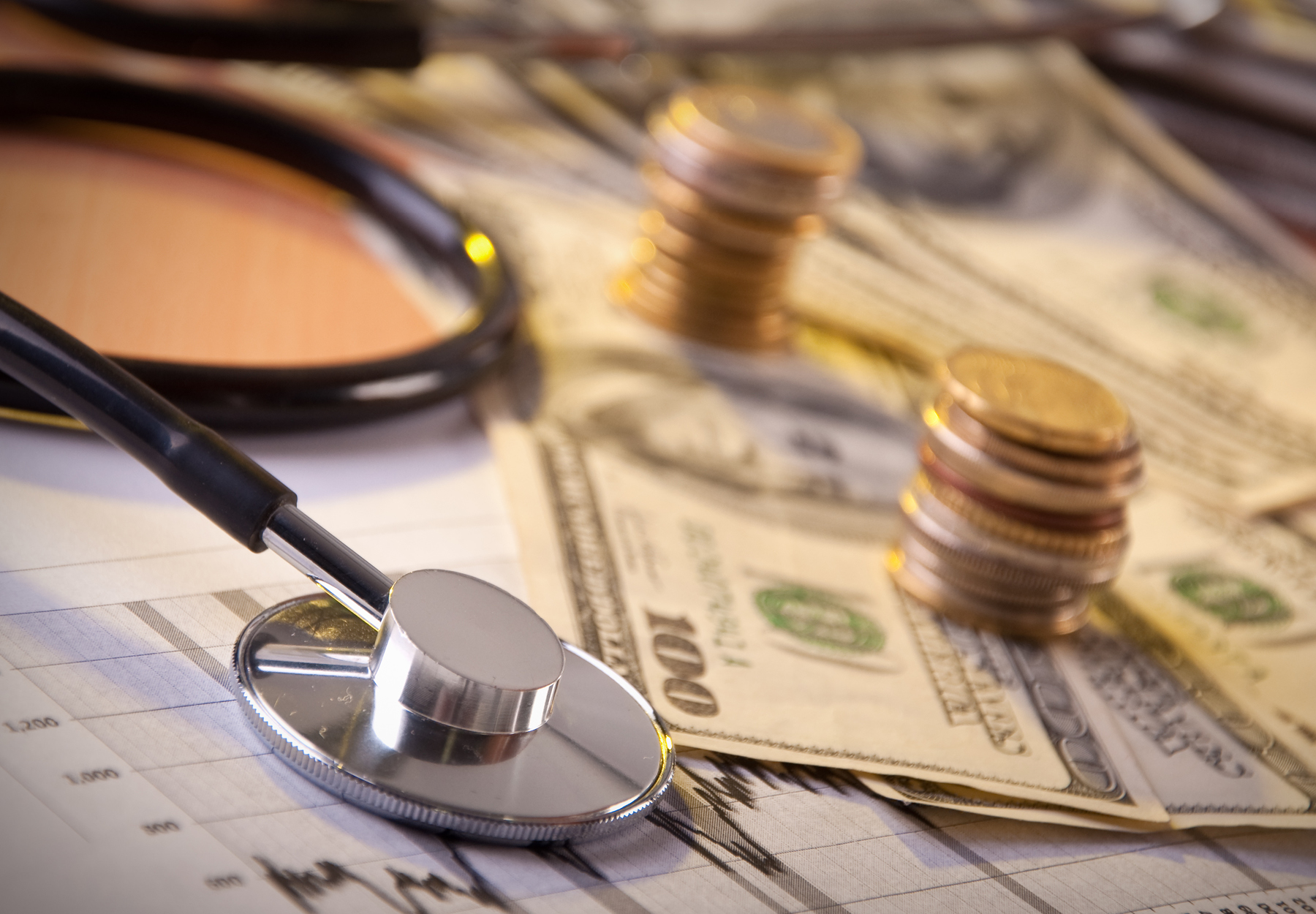 Image of U.S. paper bills and coins on a table next to a stethoscope. Healthcare fraud concept. iStock image.