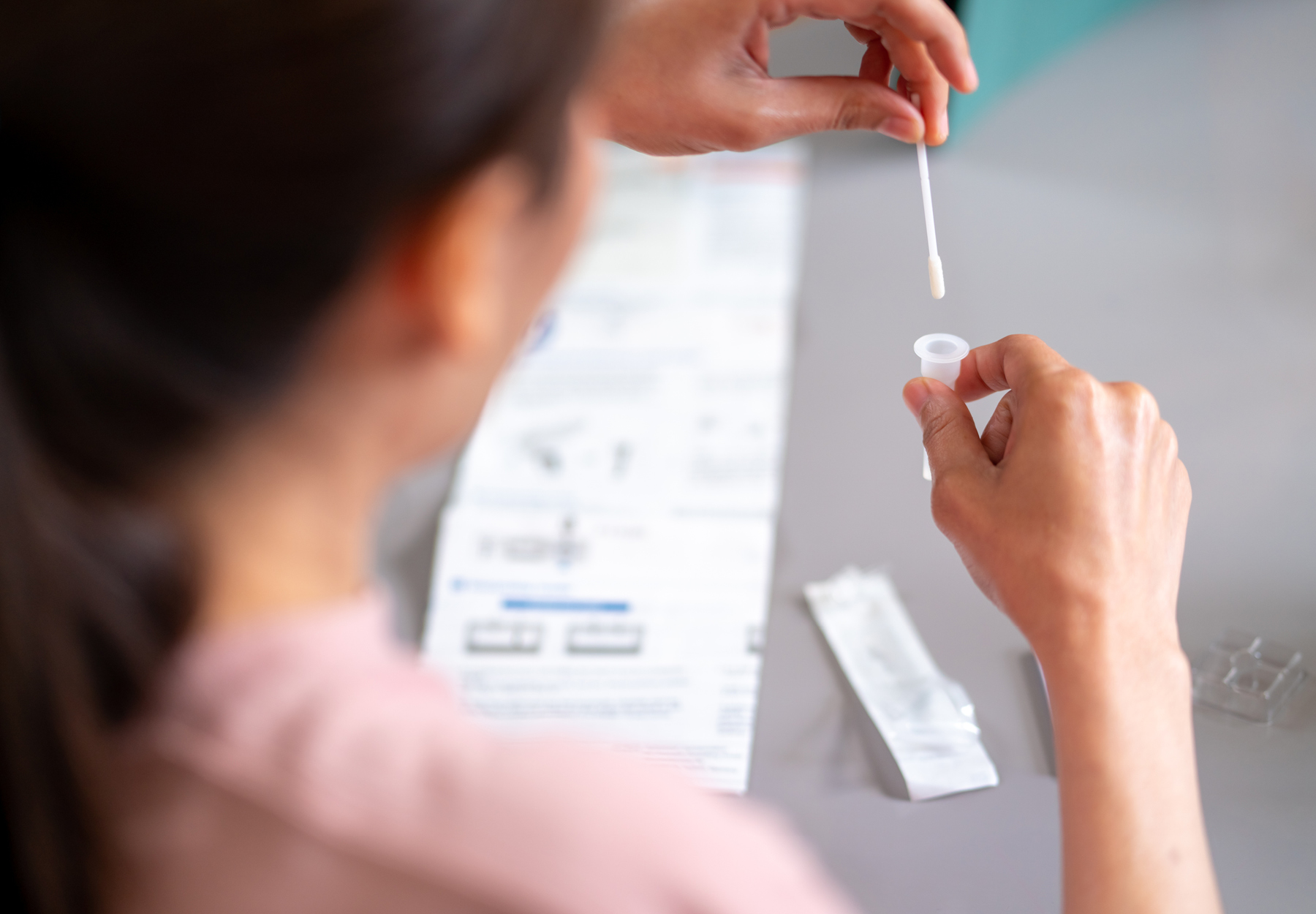 Woman in pink shirt doing at-home COVID-19 test. iStock image.