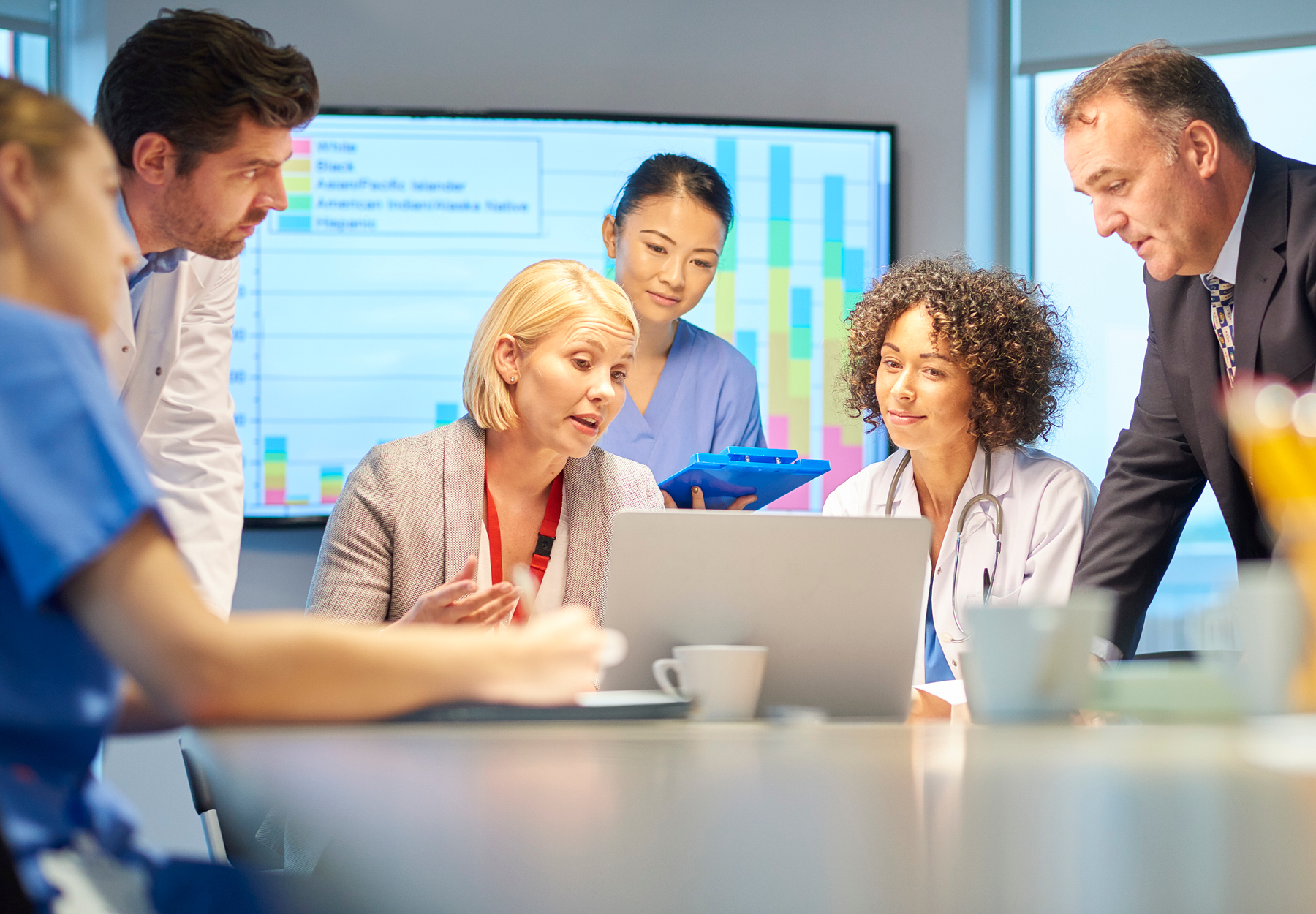 A mixed group of healthcare professional and business people meet around a conference table.