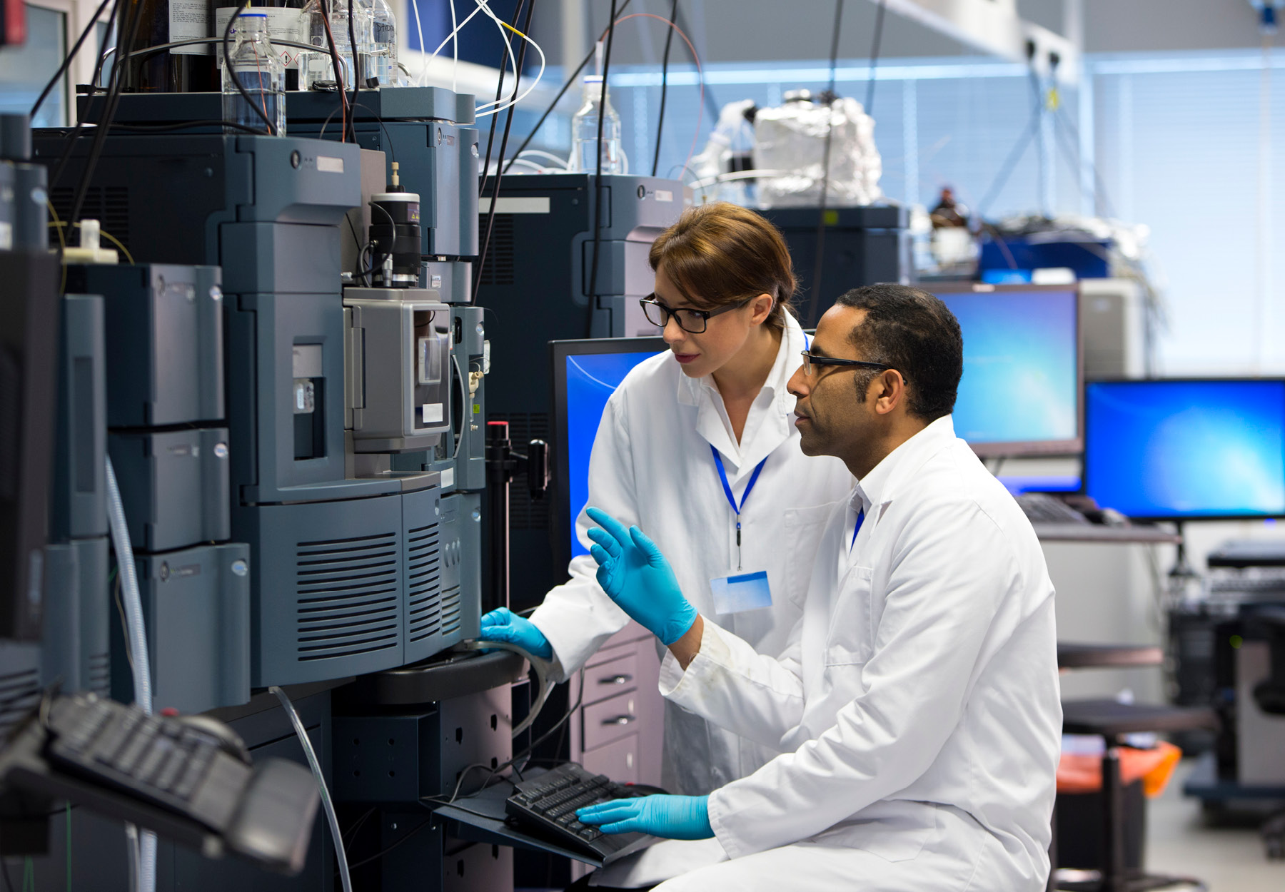 Scientists in a laboratory recording data. Both working beside a special piece of machinery called a mass spectrometer (MS) , an analytical chemistry technique that helps identify the amount and type of chemicals present in a sample by measuring the mass-to-charge ratio and abundance of gas-phase ions. Stock image.