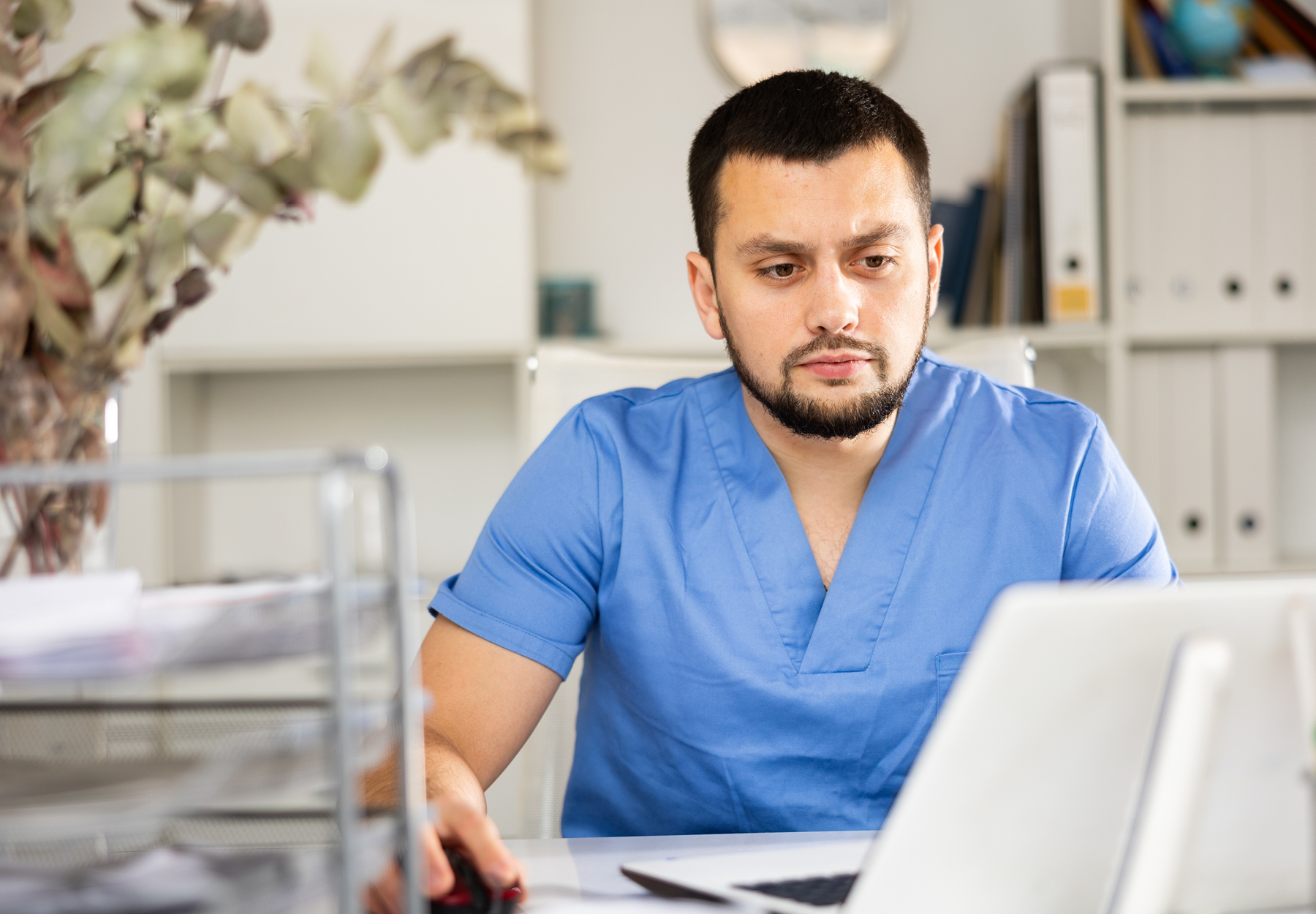 Male healthcare professional working on a laptop at his desk. Stock image.