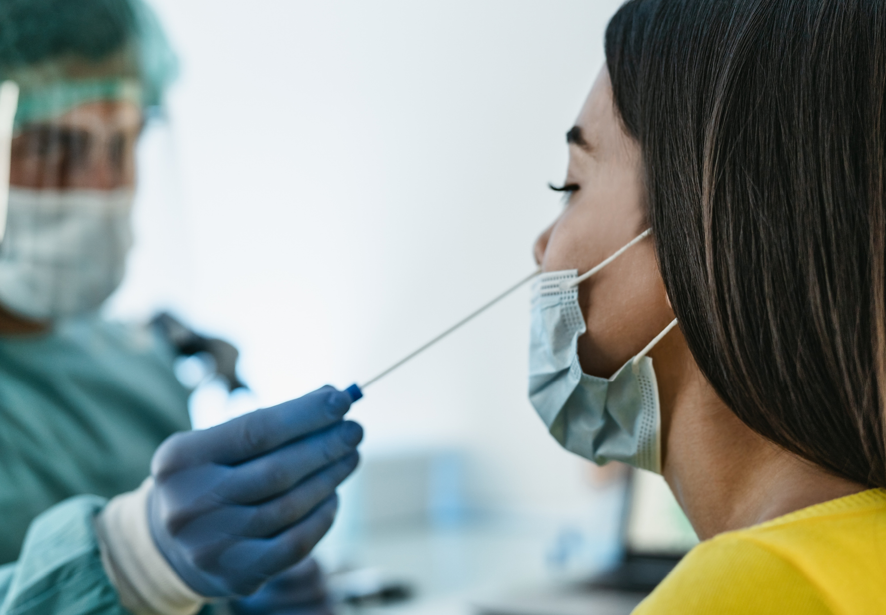 Closeup of healthcare worker in full PPE conducting a nasal swab on a woman for COVID-19 testing. Stock image.