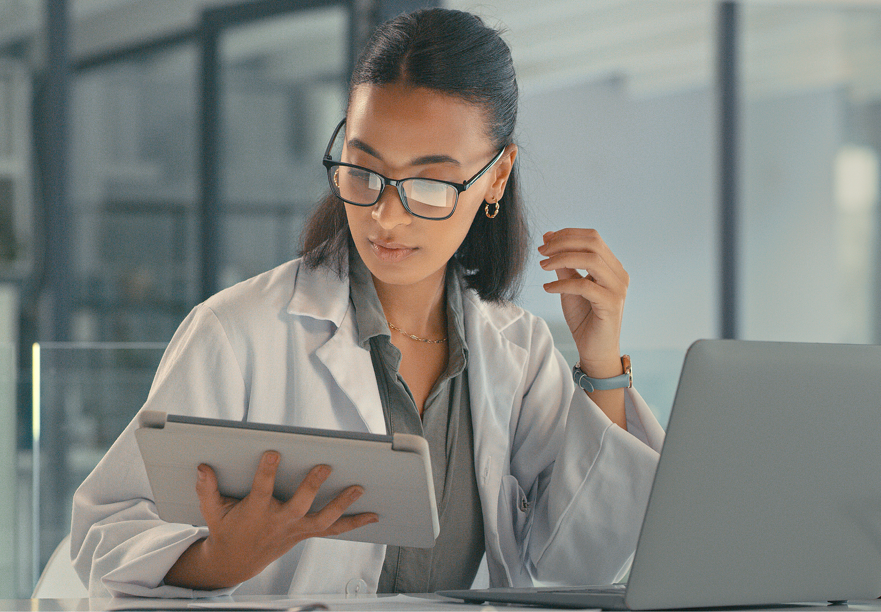 Female lab professional sits at her desk in her office looking at billing information on her tablet. iStock image.