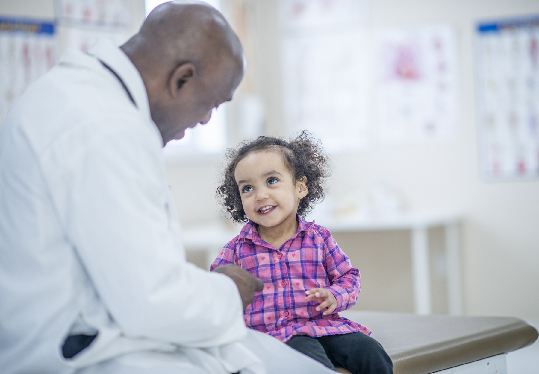 A male doctor is comforting a young girl before her checkup. They are indoors in a medical office.