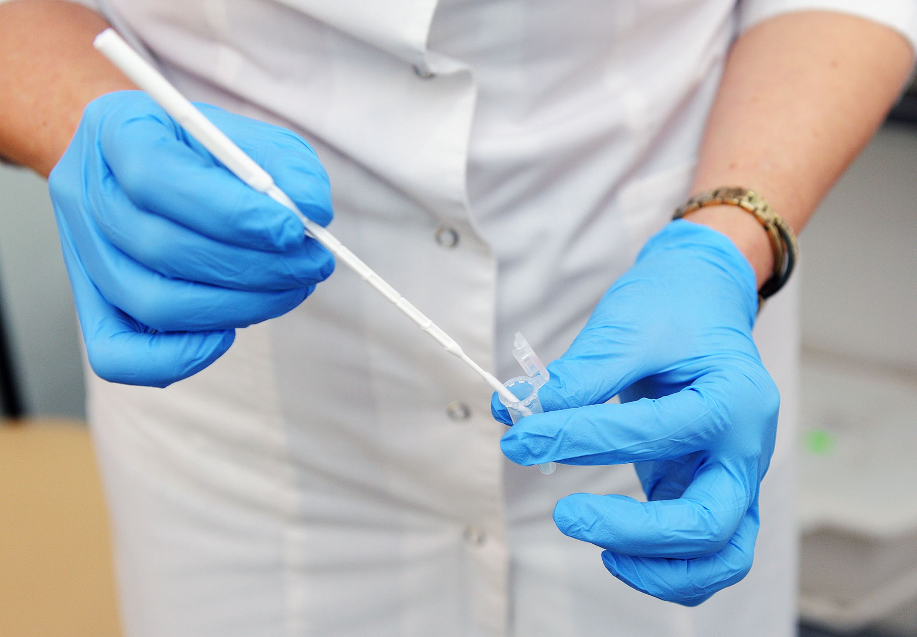 A gynecologist in blue gloves is placing a Pap smear sample in a tube.