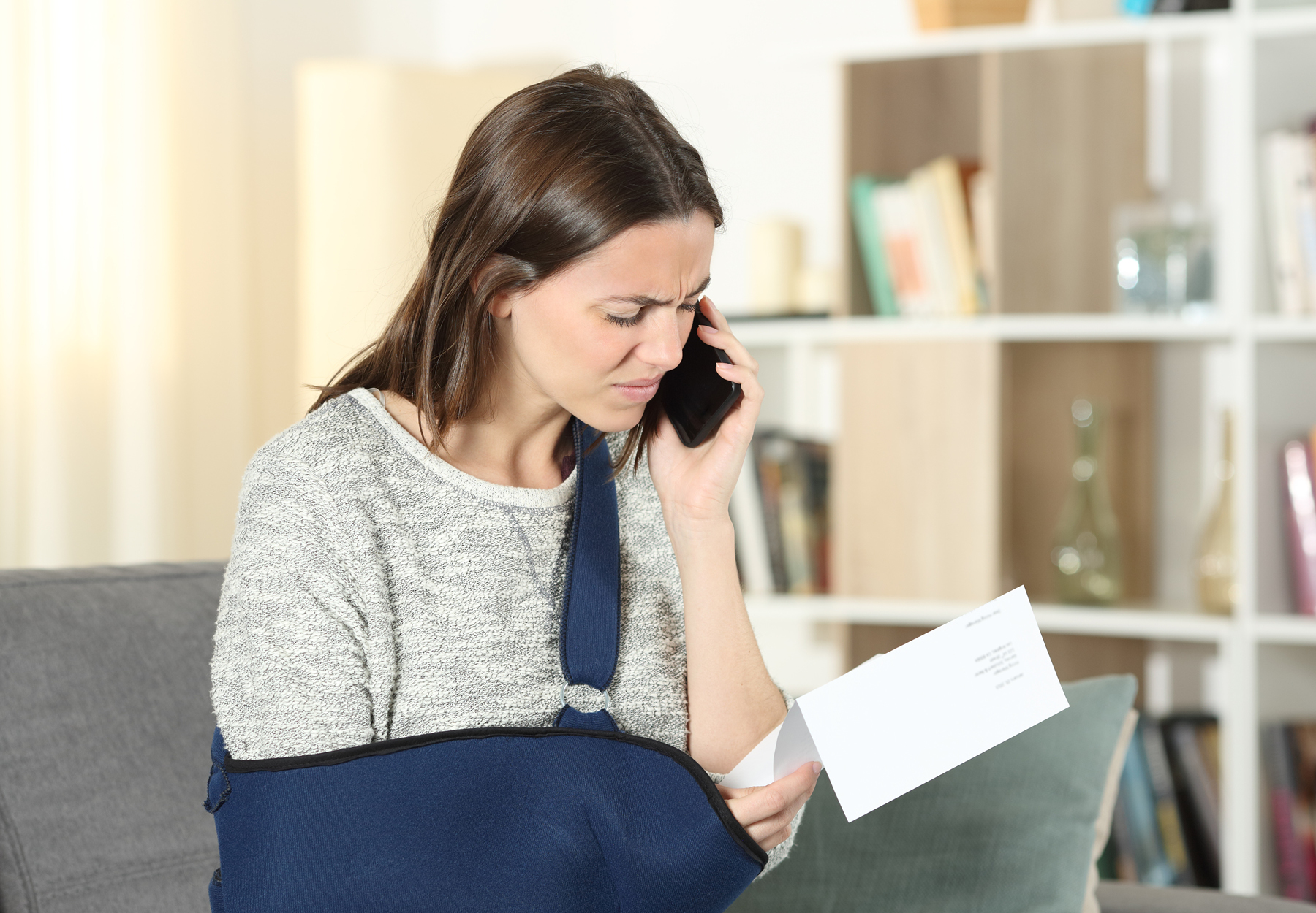 Woman with broken arm on the phone while holding a paper medical bill. Surprise medical bill concept. Stock image.