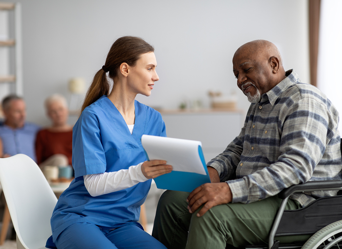 Elderly black patient looks at form shown to him by a white female healthcare professional in a medical clinic.
