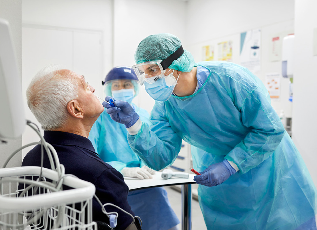 Doctor taking coronavirus sample from male patient's nose. Frontline worker is in protective workwear. They are at hospital during epidemic.