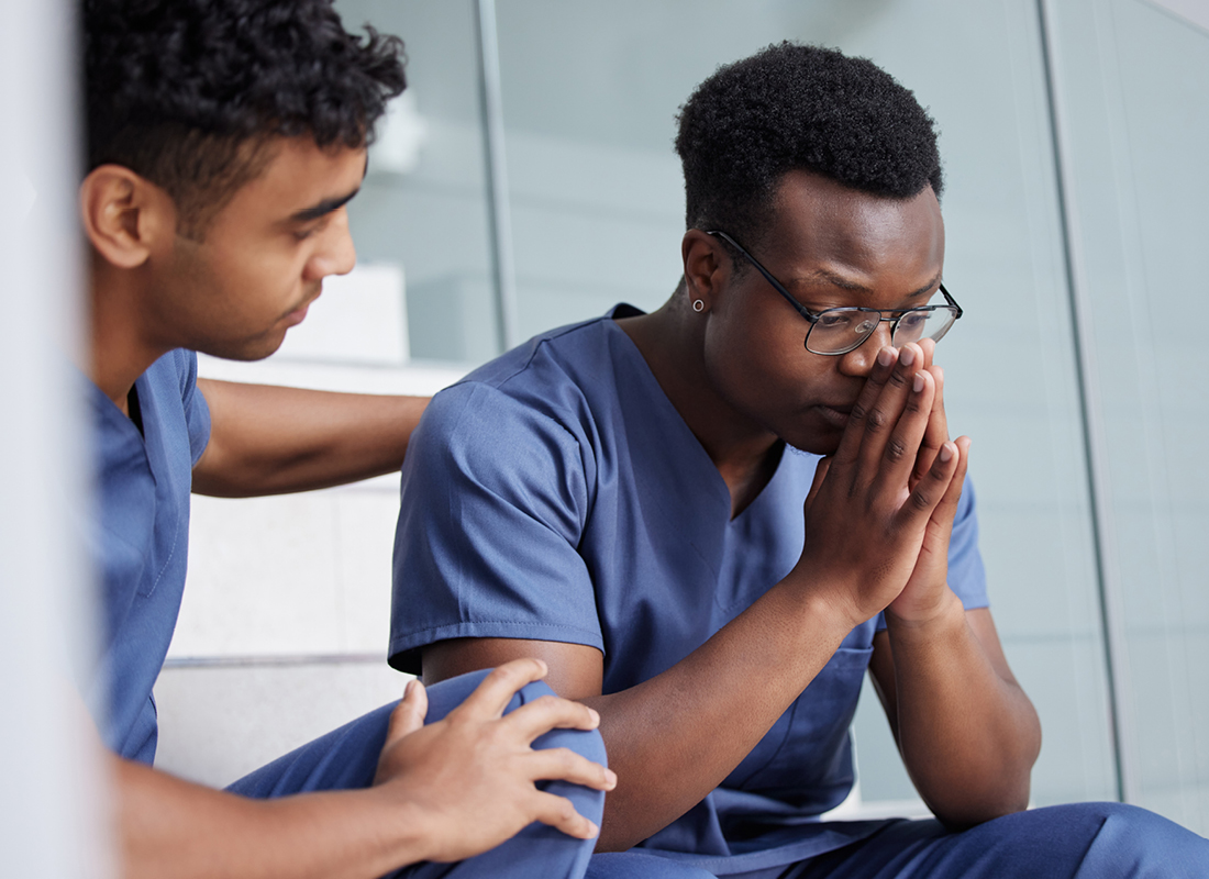 Stressed-looking male healthcare professional comforts his male colleague stock image