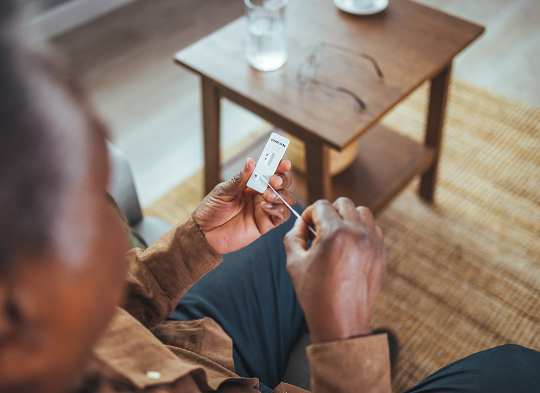 Senior man sitting, self test for COVID-19 at home with Antigen test kit. Coronavirus nasal swab test for infection. Medicine and health-related services online.