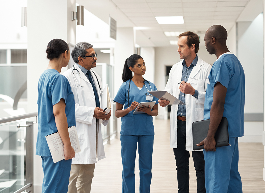 Healthcare staff of various genders and ethnicities meet in a hospital hallway.