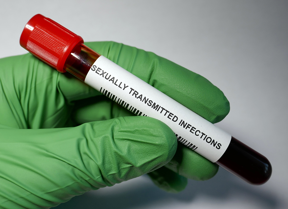 Closeup of lab professional's gloved hand holding a blood sample test tube labeled 
