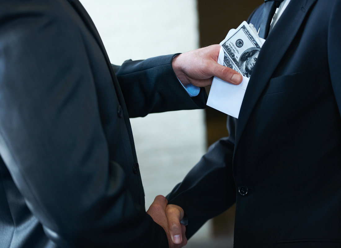 Two businessmen shaking hands while one man places money in the other's pocket. Kickbacks concept.