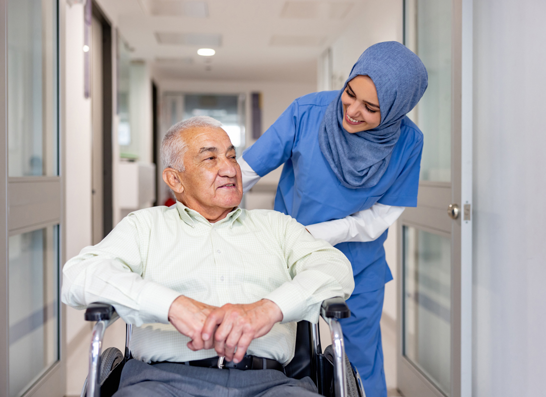 Happy Muslim nurse taking care of a senior patient leaving the hospital in a wheelchair - healthcare and medicine concepts