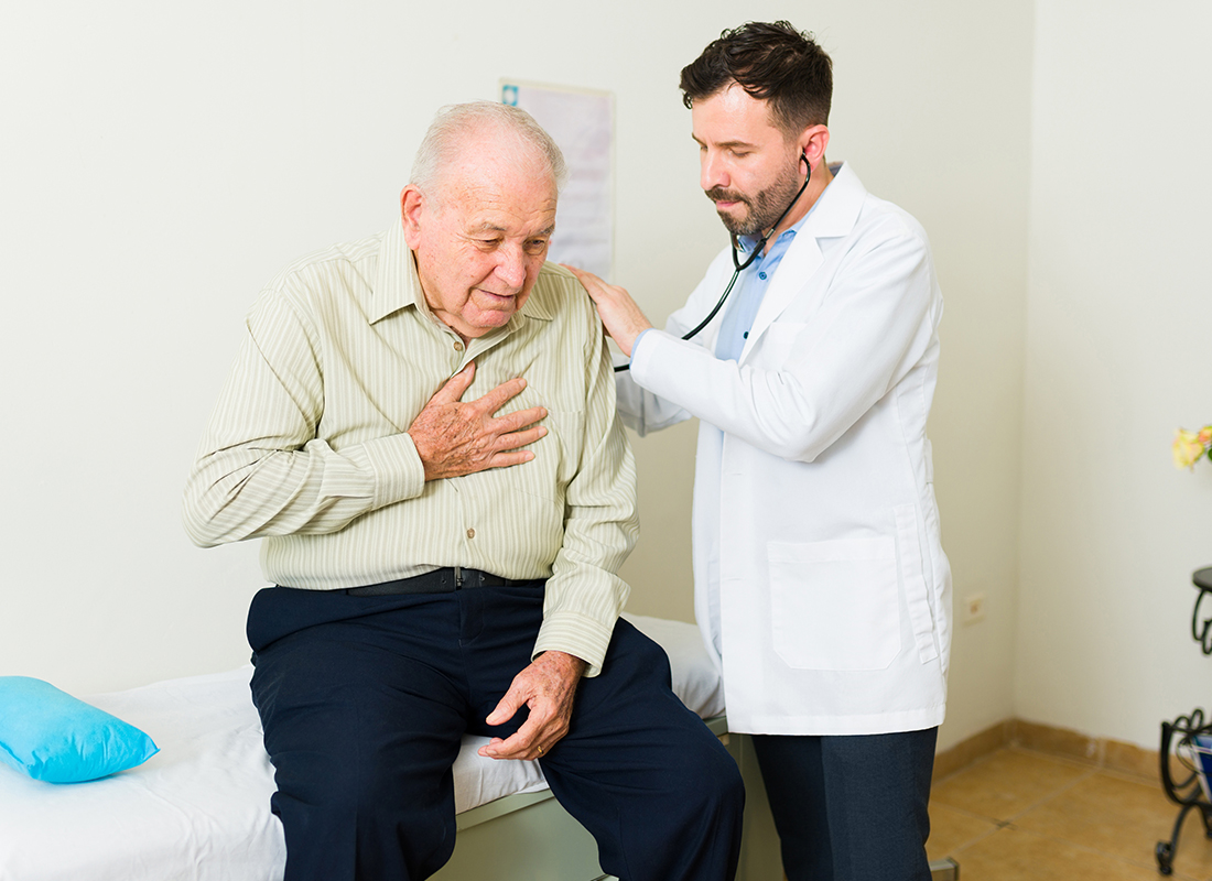 Elderly male patient who is clutching his chest meets with his male doctor, illustrating the concept of respiratory problems and breath testing.
